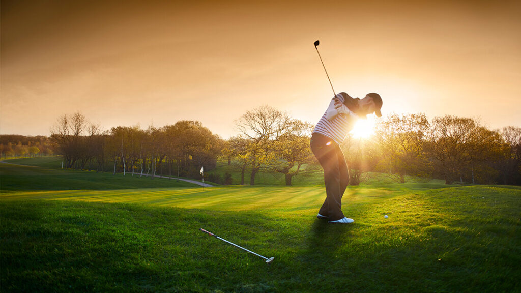 A man swinging at the sun on a golf course.