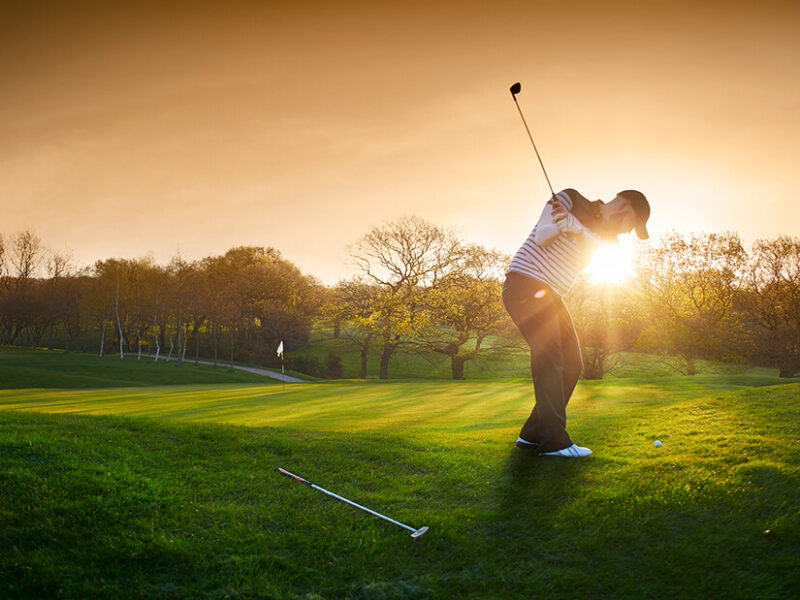 A man swinging at the sun on a golf course.