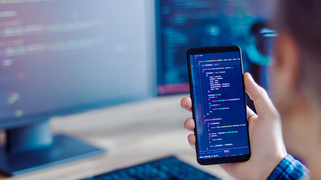 A person holding up their phone in front of a computer.