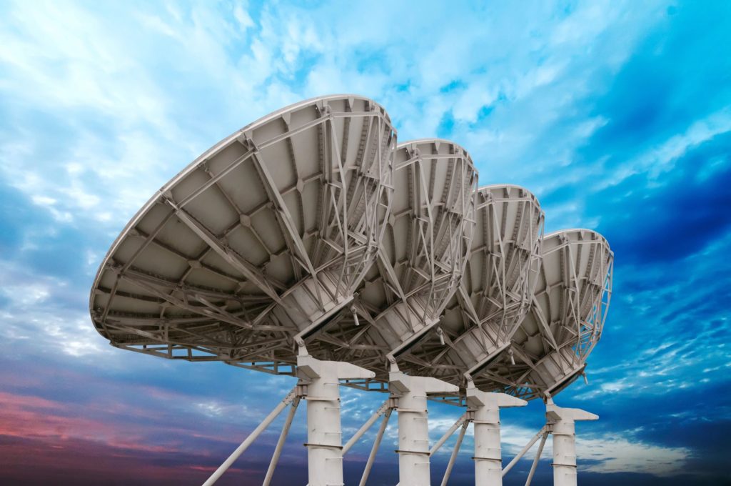 Four satellite dishes are shown against a blue sky.