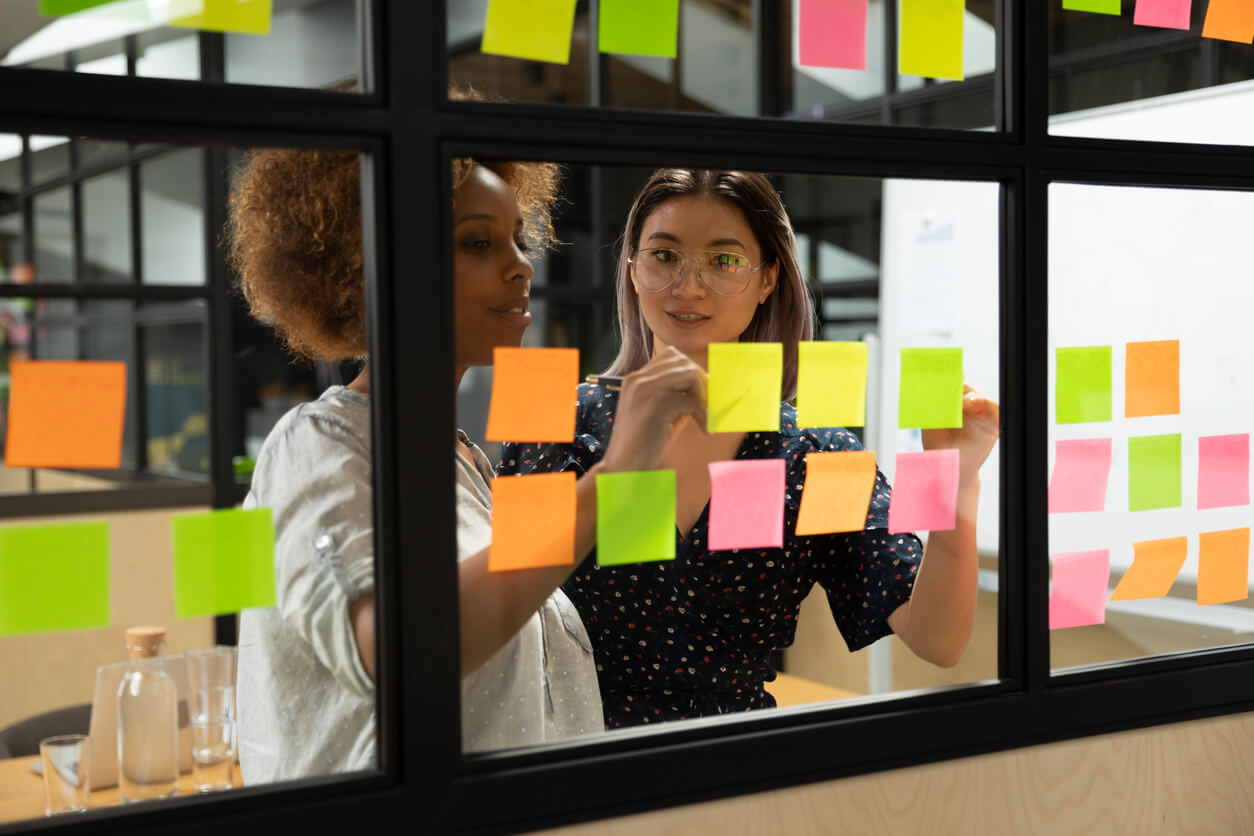 Two women looking at post it notes on a window.
