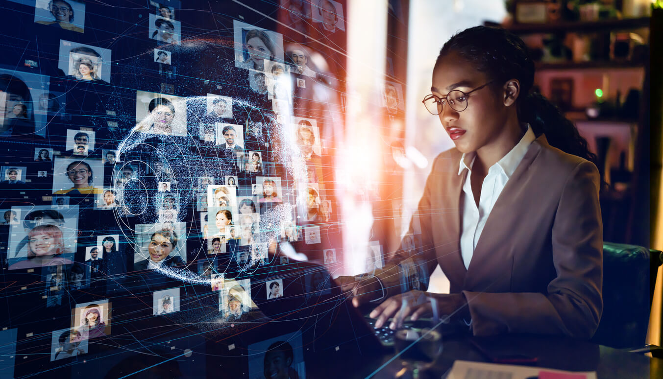 A woman sitting at her computer with many pictures of people on the wall behind her.