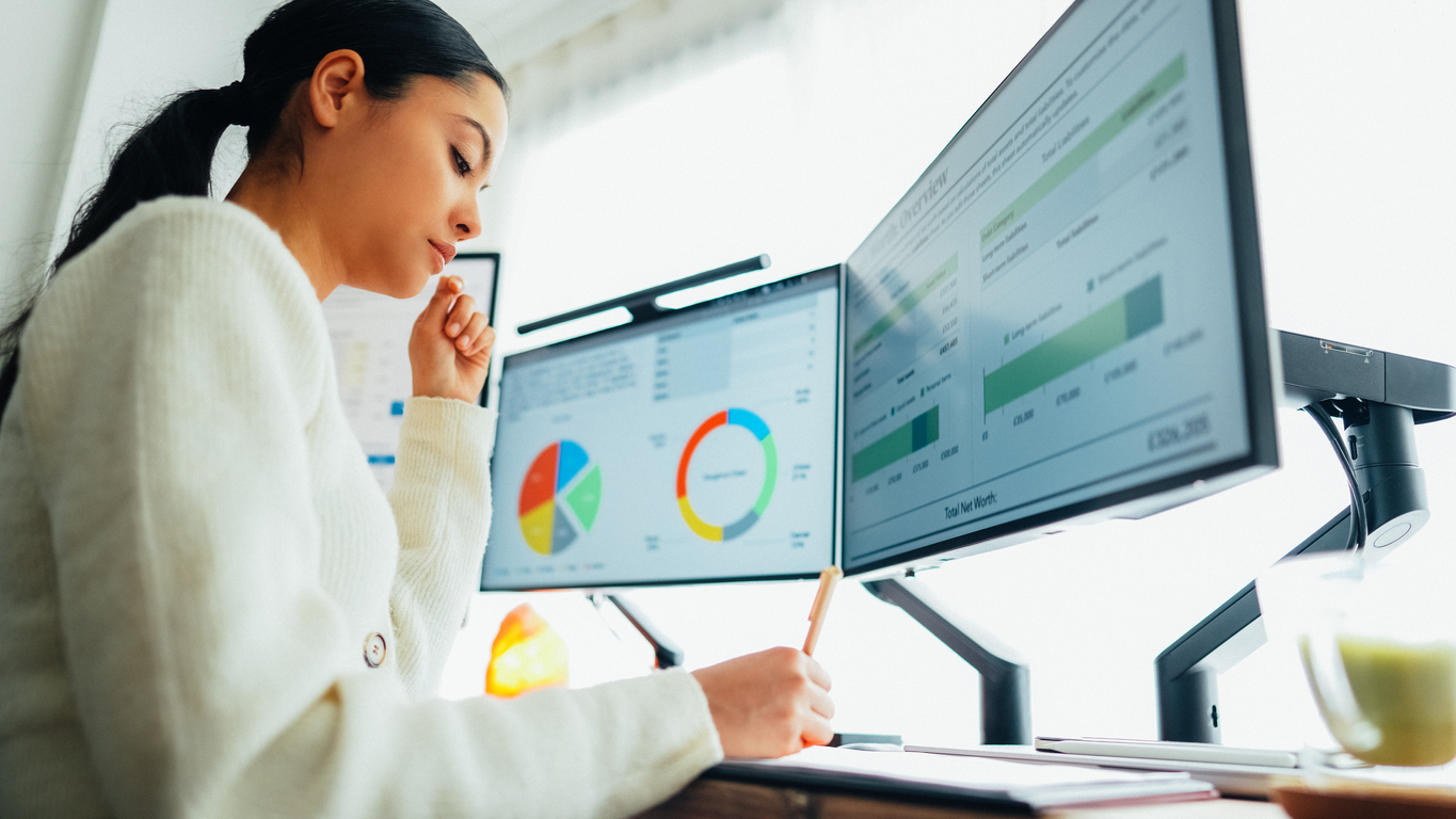 A woman sitting at her desk with two monitors.